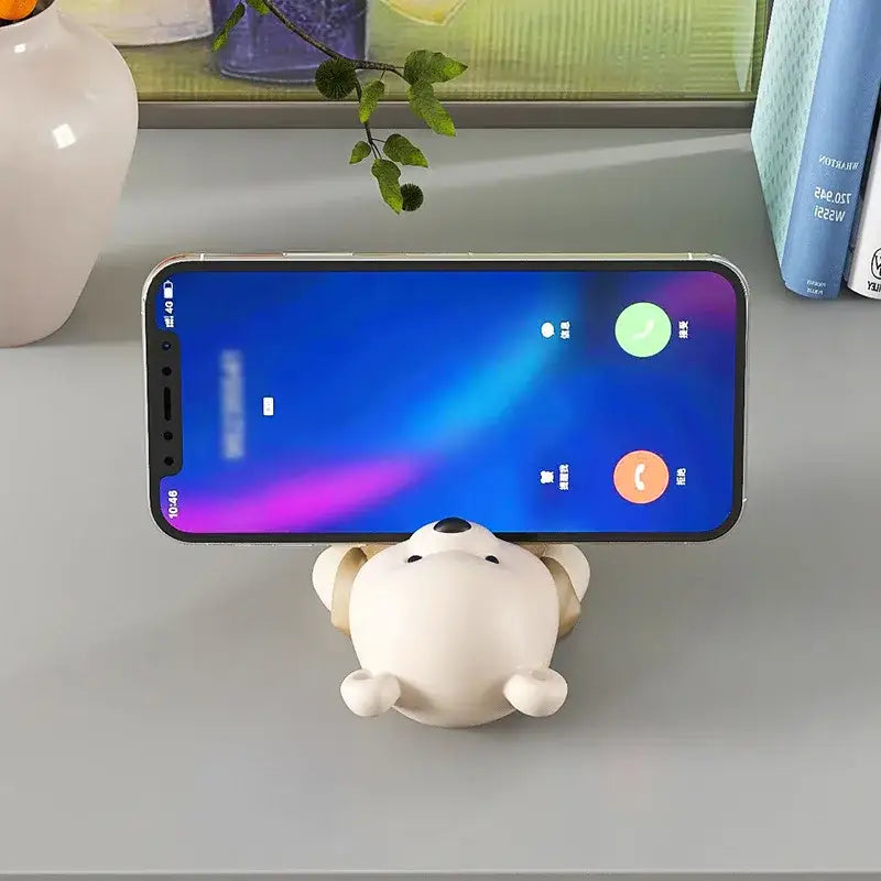 Cute cream ceramic bear cellphone stand with plush texture and rounded ears holding an iPhone on a desktop