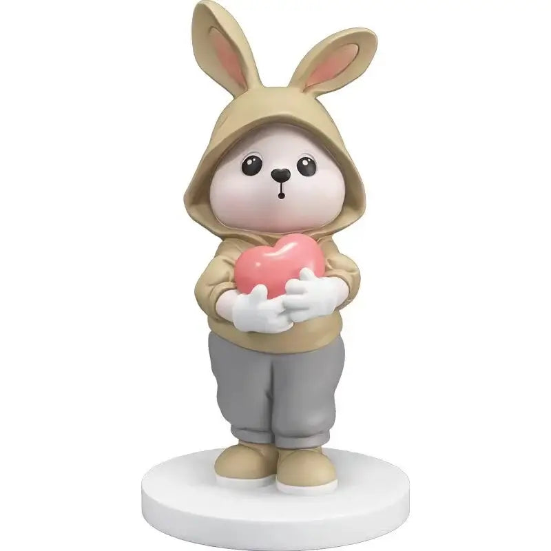 Cute beige rabbit desk figurine wearing a hooded sweatshirt holding a pink heart for home decor use