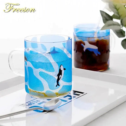 Blue glass coffee mug with black orca and white waves featuring a clear handle for heat resistant tea and coffee use