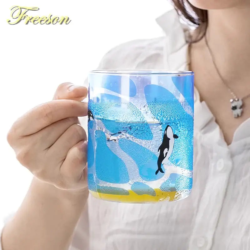 Blue glass coffee mug with black and white orca design and yellow base heat resistant for kitchen use