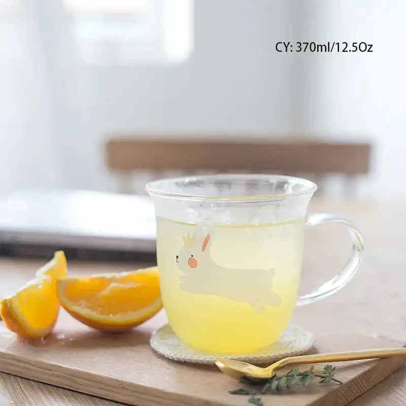 Clear glass coffee mug with a cute white bunny design and transparent handle filled with yellow liquid for tea or coffee