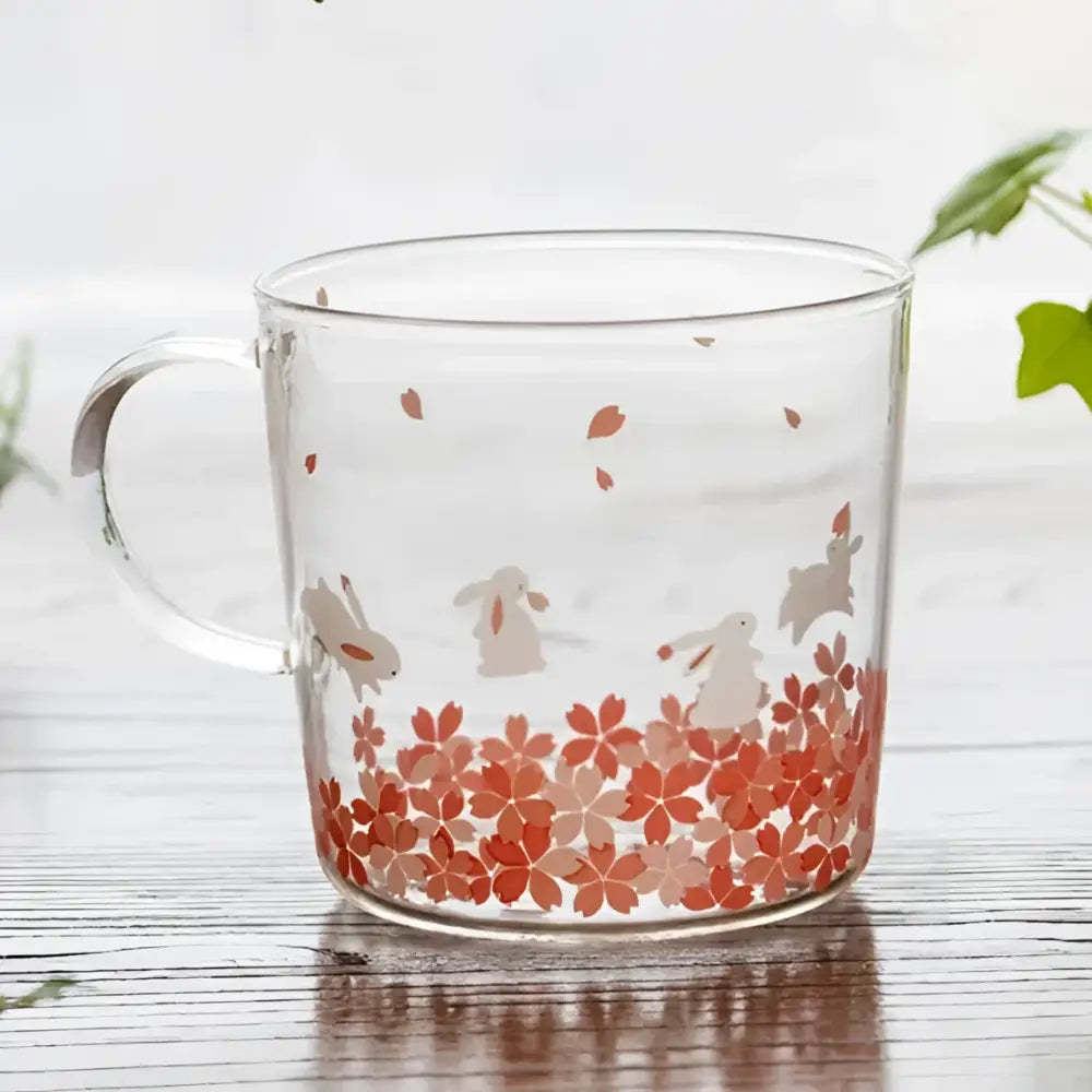 Clear glass coffee mug with delicate pink cherry blossom patterns and white rabbit silhouettes heat resistant for tea and coffee
