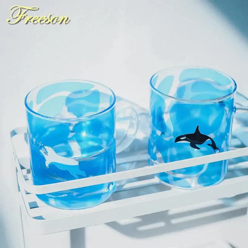 Clear blue glass coffee mugs with black and white orca illustrations by freeson for heat resistant kitchen use