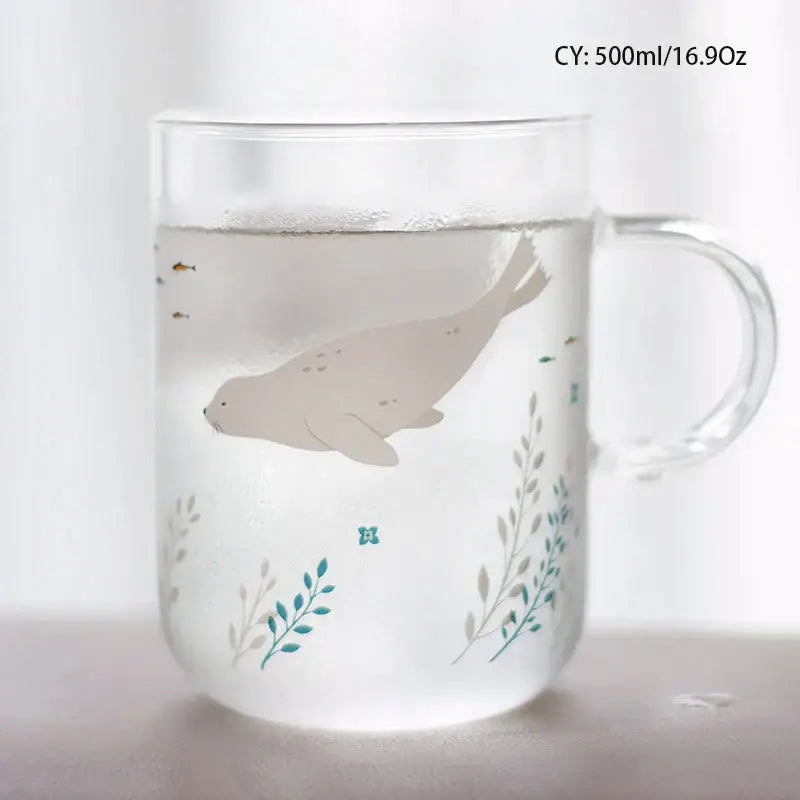 Clear glass coffee mug with light gray seal illustration among teal aquatic plants, heat resistant for kitchen use