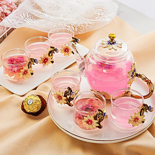Clear glass teapot set with golden floral handles and lid filled with pink liquid from daisy enamel pink crystal glass set