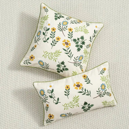 Cream-colored cushion cover with daisy floral embroidery in yellow blue and green hues and olive-green piping by decorbites