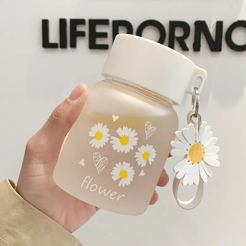 A translucent white daisy flower glass water bottle with yellow daisies and a dangling charm by decorbites