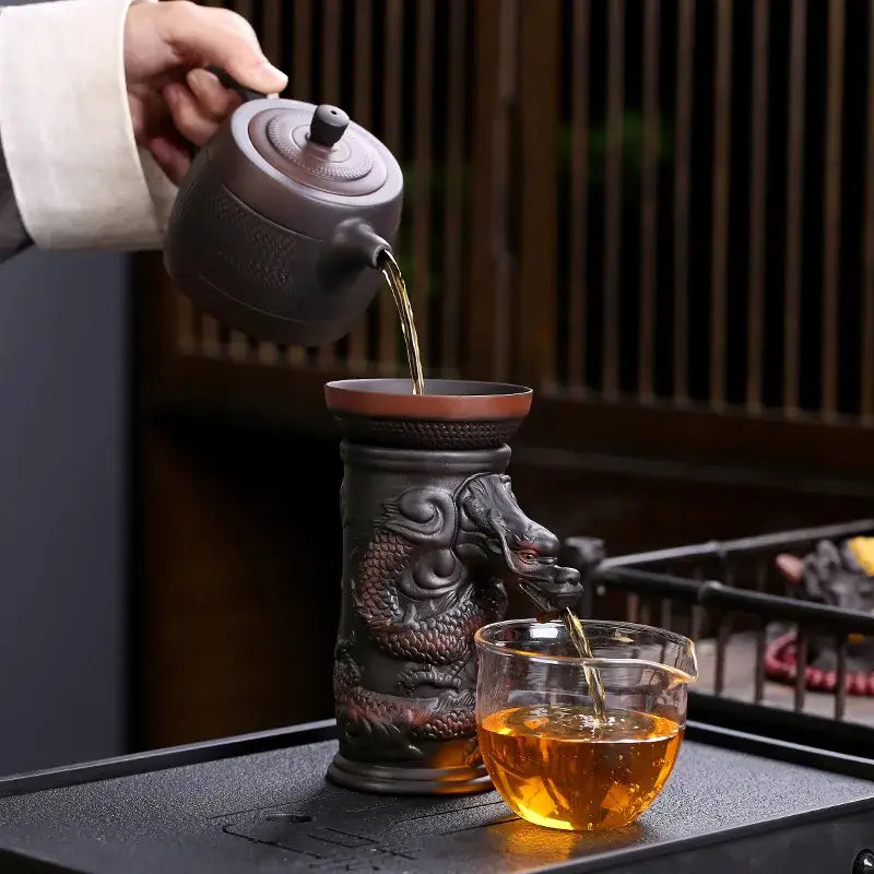 Dark brown ceramic dragon tea leaf funnel filter teapot with intricate carvings pouring into a glass cup decorbites dragon tea