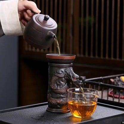 Dark brown ceramic dragon tea leaf funnel filter teapot with intricate carvings pouring into a glass cup decorbites dragon tea