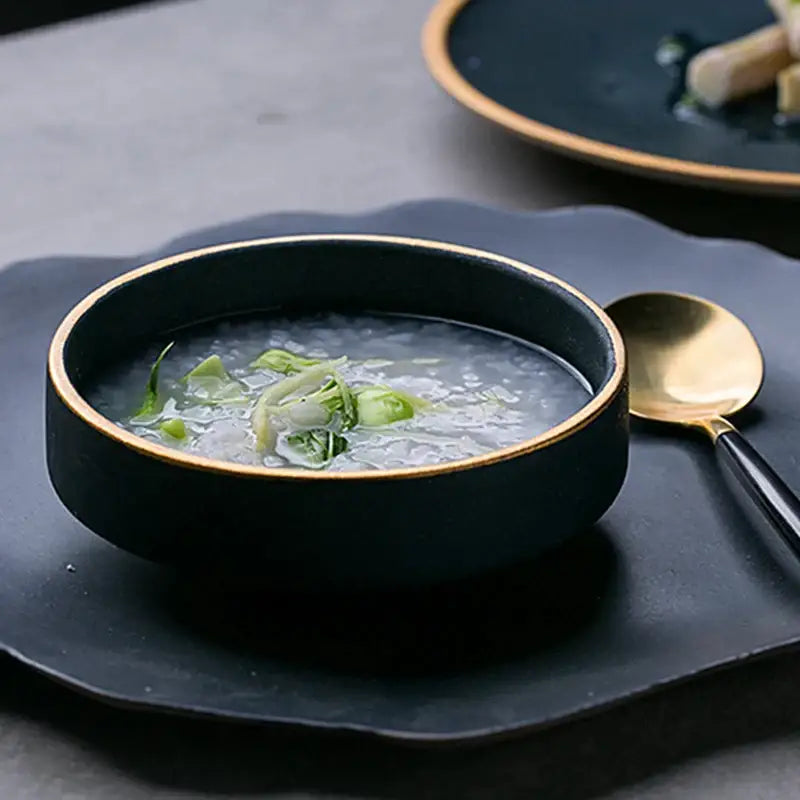 Black ceramic bowl with gold rim filled with clear soup and green garnish from decorbites ceramic western dinnerware set