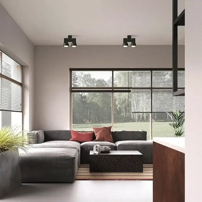 Modern white surface mount downlight installed above a gray sectional sofa with plush cushions and reddish-pink pillows