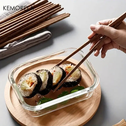 A pair of natural wooden chopsticks picking up sushi from a clear glass container enhancing the dining experience