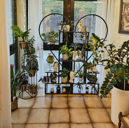 Black metal heart shaped plant display stand with six tiers holding potted plants and decorative figurines by decorbites