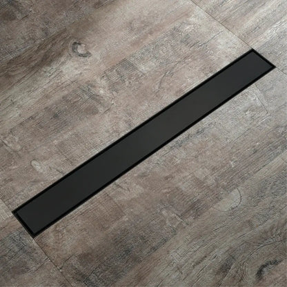 Black rectangular floor drain with sleek modern design set into gray wood-grain tiles for rose gold bathroom use