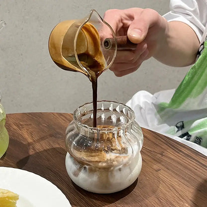 A clear glass pitcher pouring dark coffee into a ribbed cocktail glass from the 650ml latte ribbed glass set