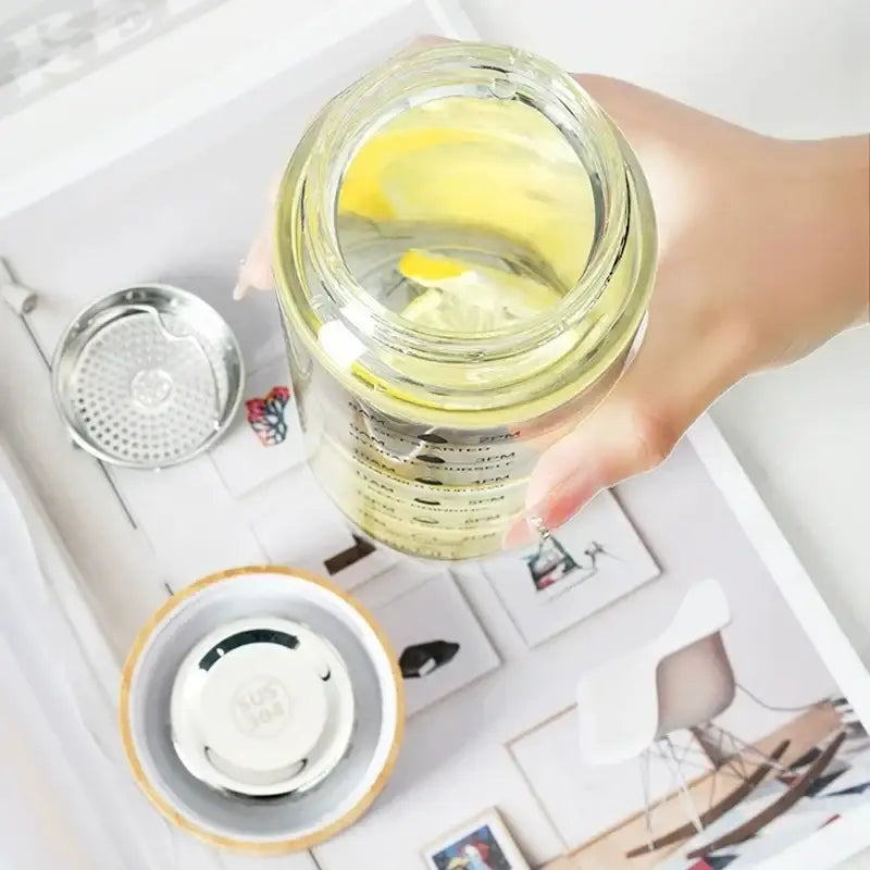 Clear glass water bottle with bamboo lid and stainless steel infuser filled with lemon-infused water from DecorBites™