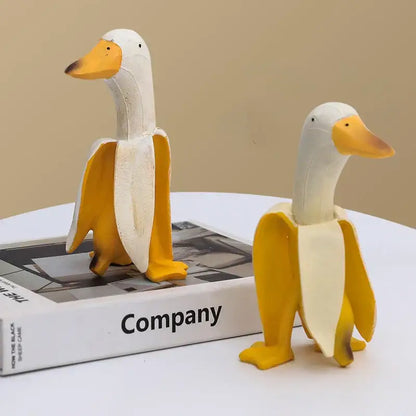 Two whimsical white and yellow decorative figurines designed as abstract banana duck sculptures for home decoration