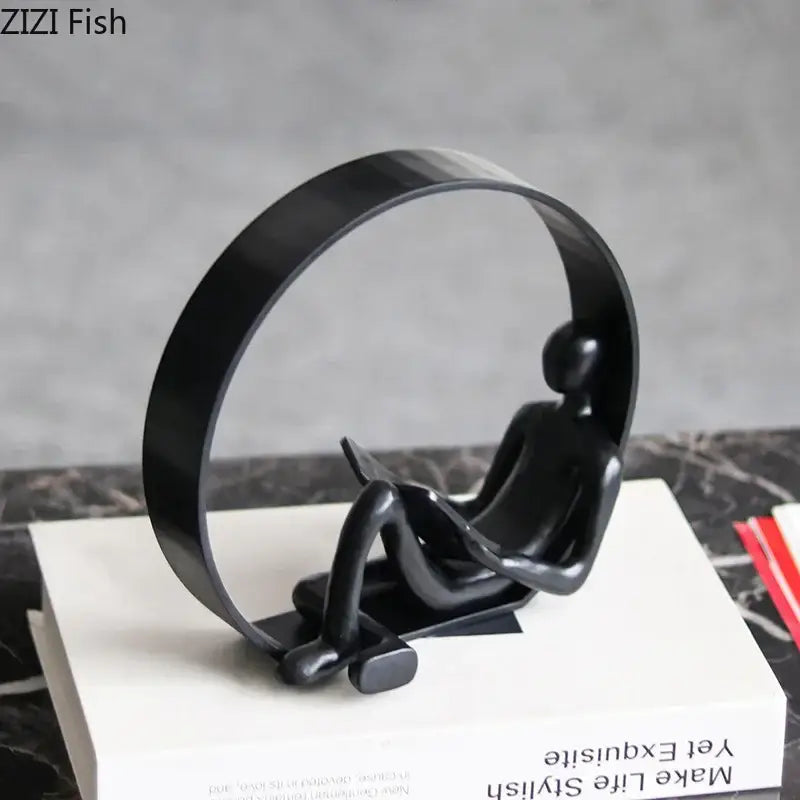 Black glossy resin figurine of a seated human figure holding an open book resting against a circular arc decorbites abstract black characters