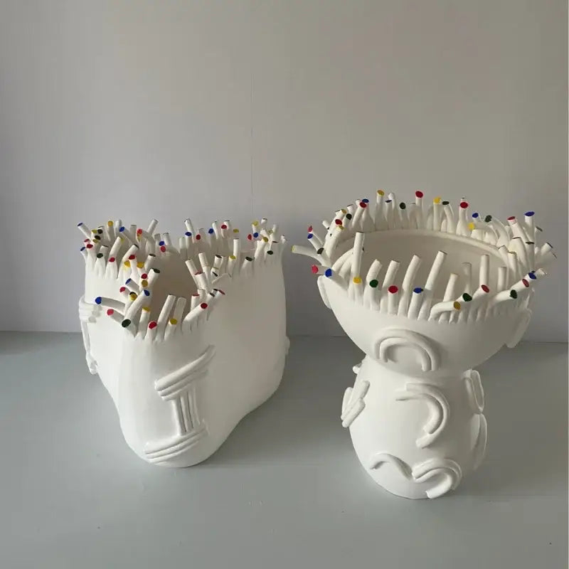 Two white ceramic vases shaped like stylized heads filled with colorful matchsticks from decorbites abstract coral shapes flower pots