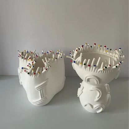 Two white ceramic vases shaped like stylized heads filled with colorful matchsticks from decorbites abstract coral shapes flower pots