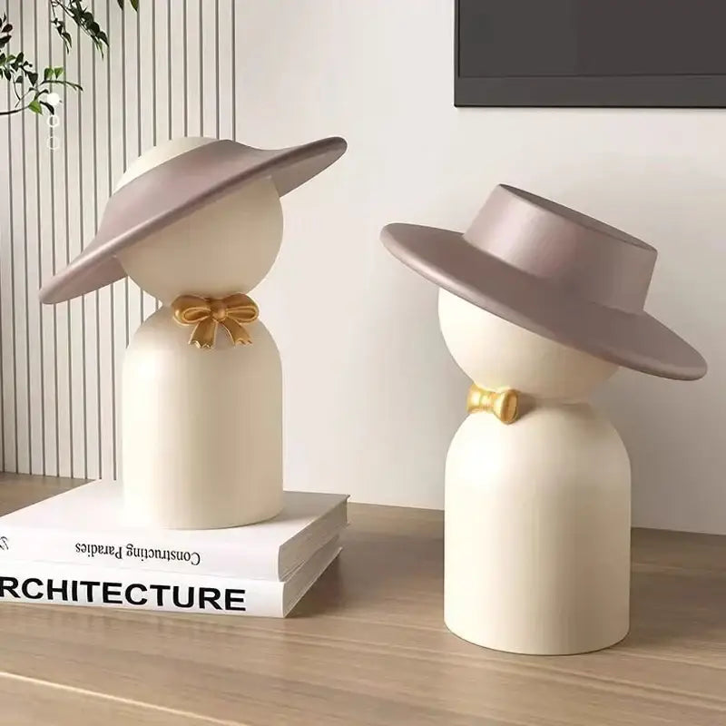 Cream-colored ceramic decorbites abstract couple bust sculpture with wide-brimmed hats and gold bows for stylish decor