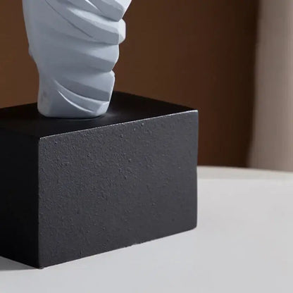 A sleek light gray twisted ceramic decorbites abstract dancer figure on a textured black square base for modern decor