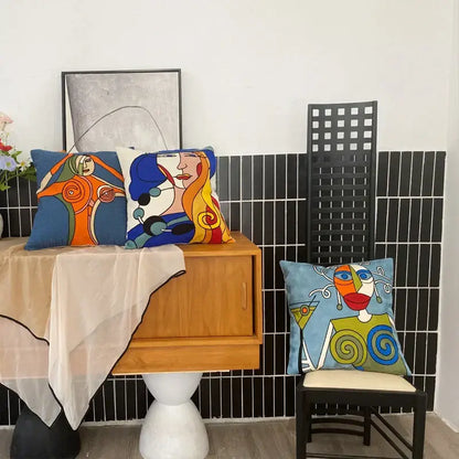 Three colorful decorbites abstract embroidery pillowcases 45x45cm with stylized faces on wooden cabinet and chair