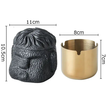 Black textured resin portraits cement ashtray shaped like a man’s head next to a gold-toned metal cylindrical ashtray