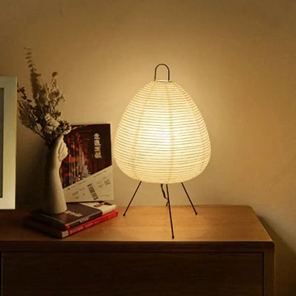 Warmly glowing akari noguchi table lamp with ribbed off-white rice paper shade and black metal tripod base for home décor