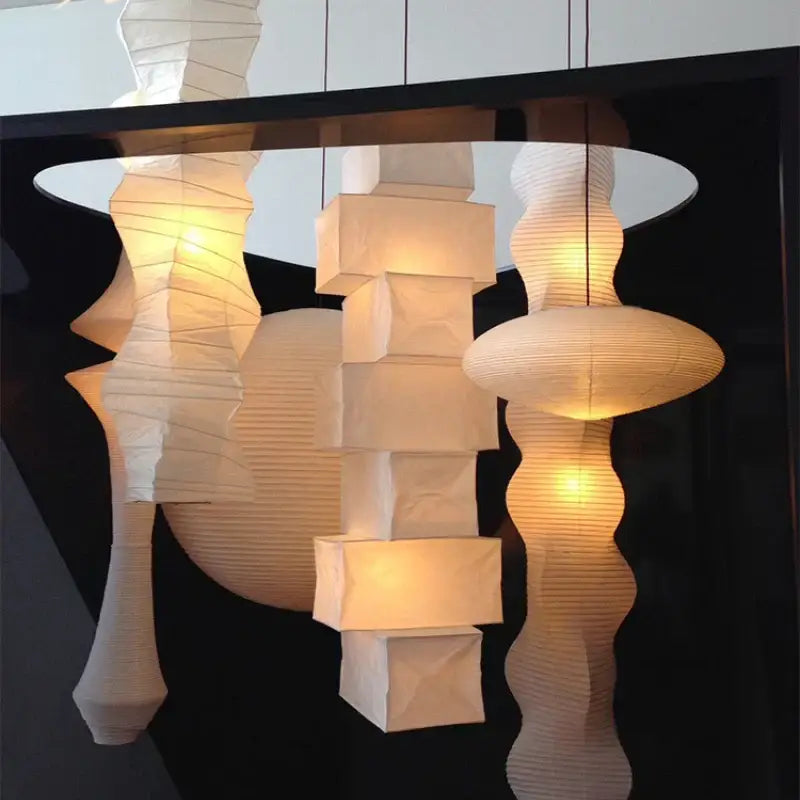 A collection of white akari rice paper pendant lamps with geometric and organic shapes illuminated for living room use