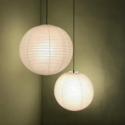 Two off-white spherical decorbites™ akari vintage rice paper pendant lights hanging against a muted green wall