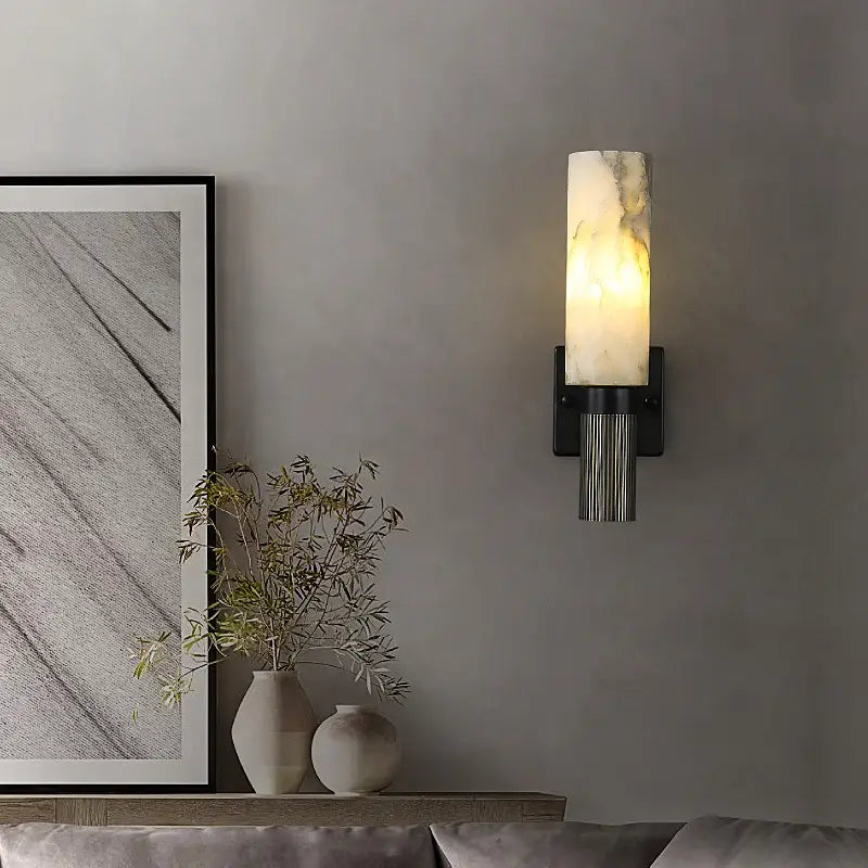 A modern alabaster copper wall lamp with a cylindrical white marble shade and black ridged metal base for living room use
