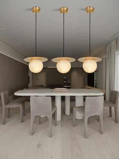 Three modern alabaster marble pendant lights with gold fixtures and frosted globes for luxury dining room décor