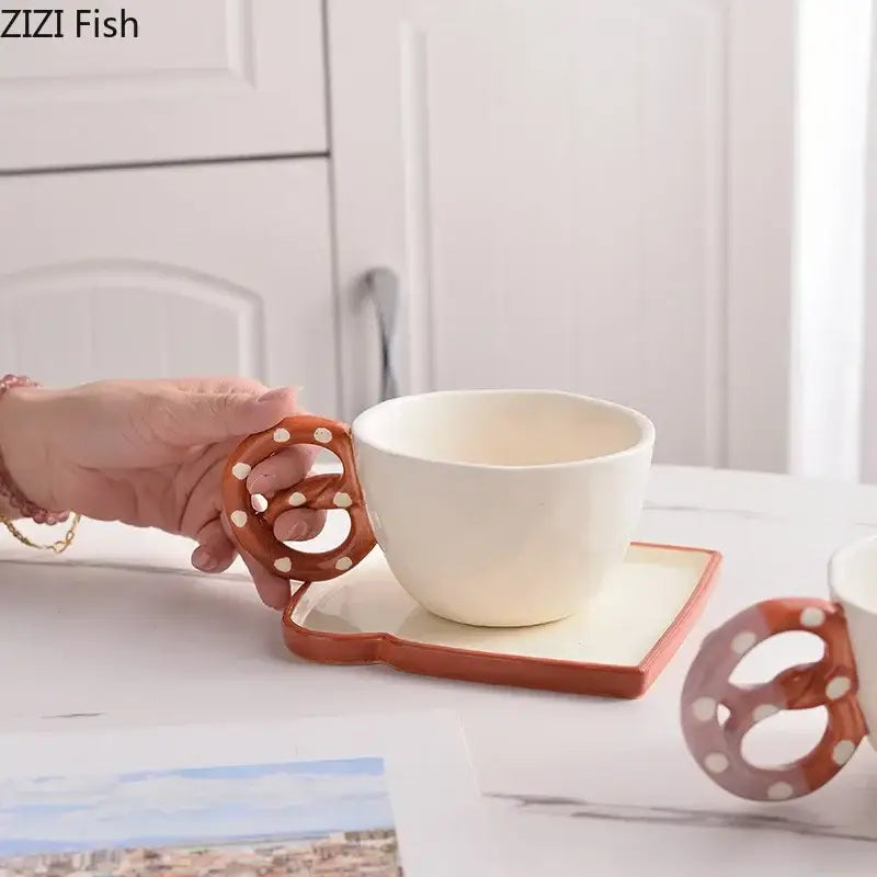 White ceramic alkali water biscuit mug set with pretzel-shaped polka dot handle on matching rectangular saucer