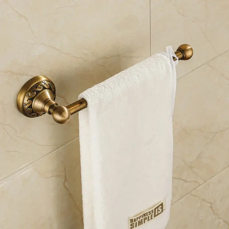 DecorBites™ aluminium wall mounted towel holder in antique brass with ornate detailing holding a white towel