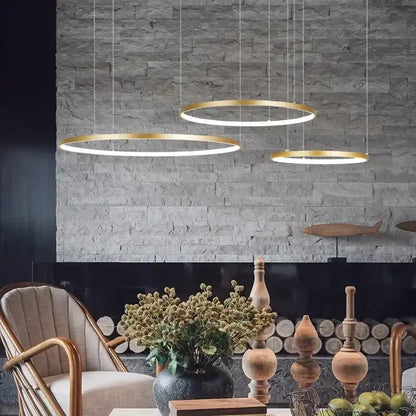 Three modern gold-toned aluminum rings led pendant lights hang from the ceiling in living room or bedroom settings