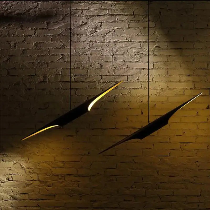 Two black decorbites aluminum tube pendant lights with glowing yellow edges hang on a textured brick wall