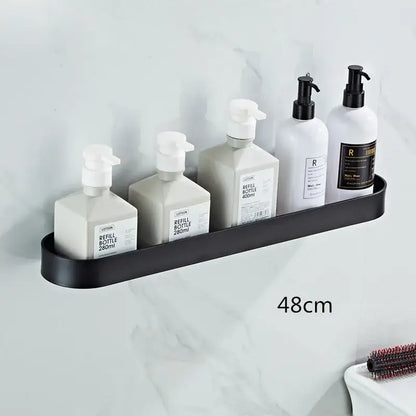 Black matte aluminum bathroom shelf with towel bar and corner storage shelf holding five white pump bottles
