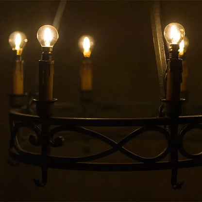 Dark wrought iron chandelier with multiple glowing amber glass led filament bulbs suitable for dimmable outdoor use