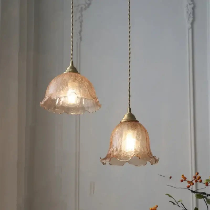 Two delicate peach-colored glass led pendant lamps with ruffled edges and brass fixtures for ambient lighting