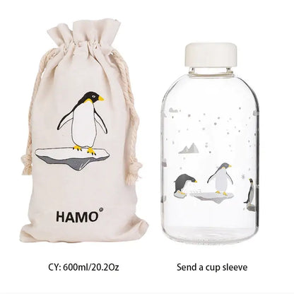 Clear glass water bottle with white cap and penguin illustration with matching beige drawstring sleeve for outdoor use