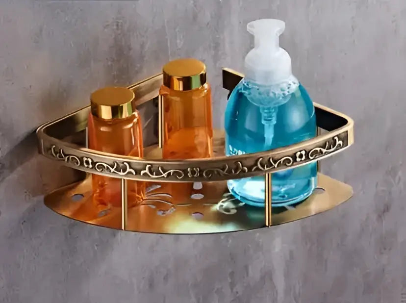 Gold-toned triangular decorbites antique bathroom shelf with ornate scrollwork holding amber bottles and bath hardware
