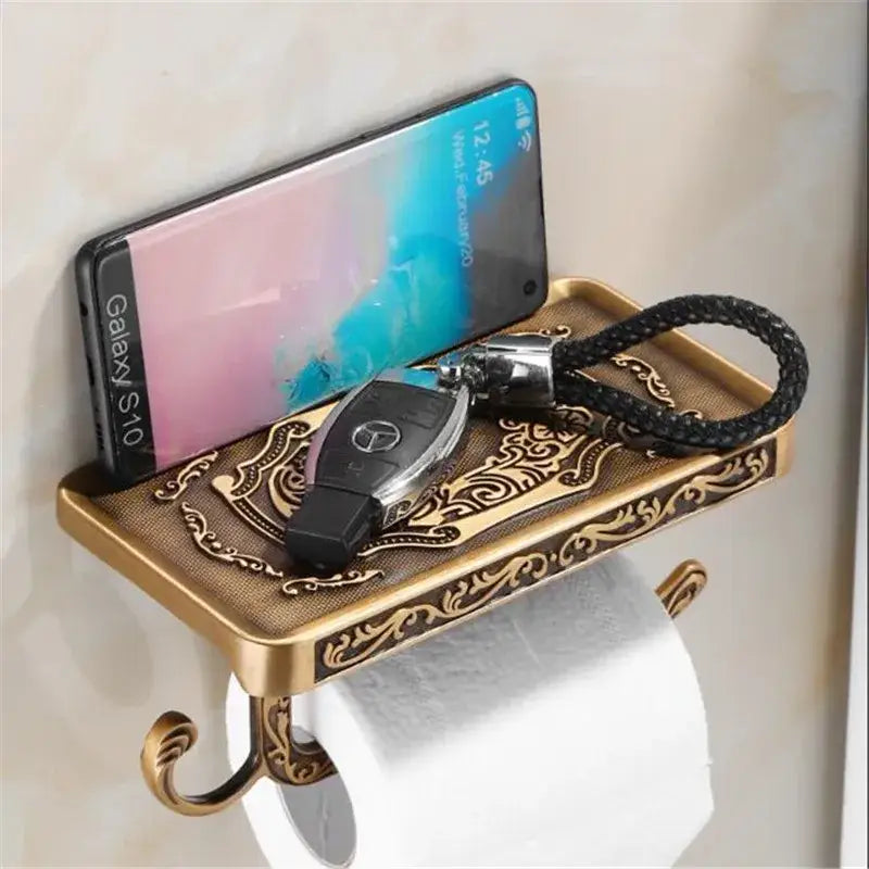 DecorBites™ antique black toilet paper holder with ornate brass shelf holding smartphone and key fob for bathroom use