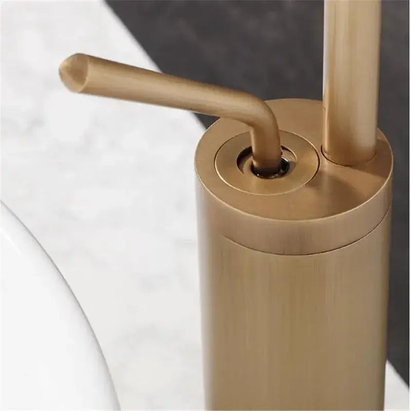 Brushed gold-finished soap dispenser with sleek cylindrical body and curved pump handle for brass bathroom basin use