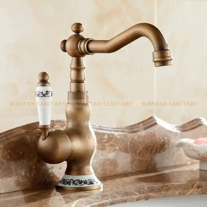 Antique brass bathroom sink faucet with white ceramic handle and base featuring black floral patterns by DecorBites