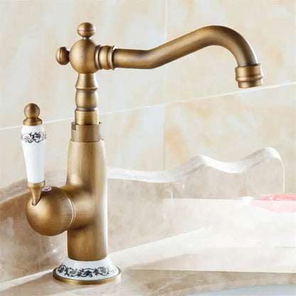 Antique brass bathroom sink faucet by decorbites with curved spout and ornate ceramic handle with black floral detailing