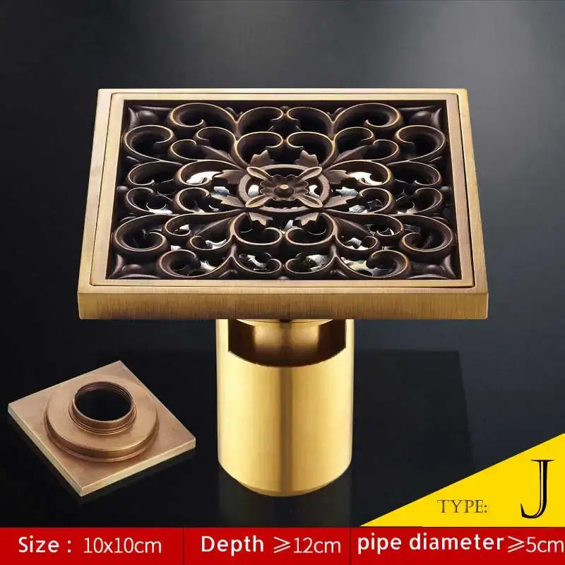 Square brass bathroom shower drain with antique brass fish style ornate floral cutout and matching cylindrical pipe
