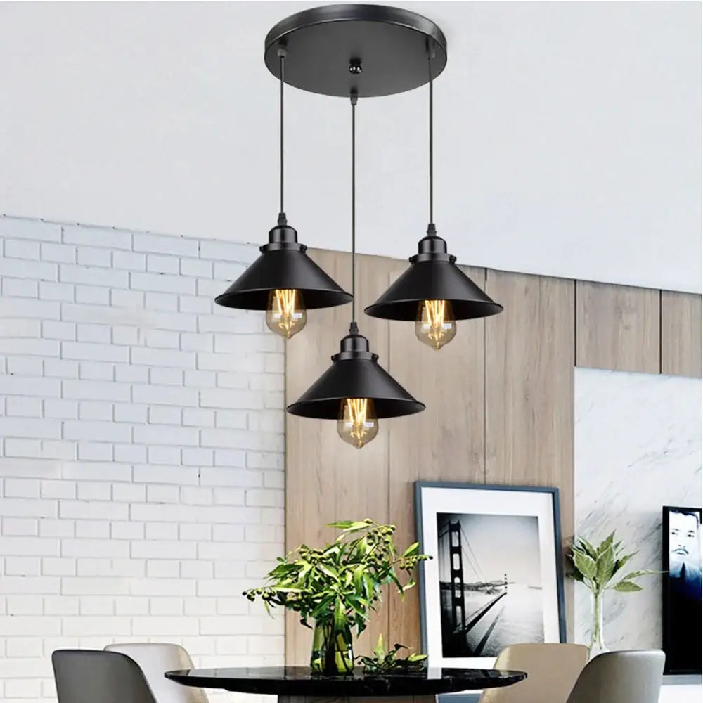 Black industrial-style pendant light fixture with three conical shades and exposed filament bulbs for antique brass kitchen