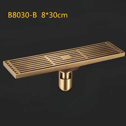 Brass-colored antique brass linear floor drain with slatted art carved cover and cylindrical mounting base for shower use