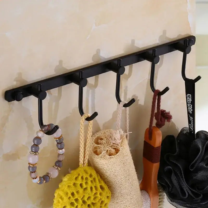 Black metal wall-mounted hook rack with five antique brass robe hooks holding bathroom items for stylish organization